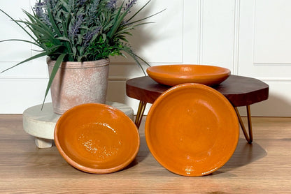 Three terracotta bowls on a wooden surface with a plant in the background.
