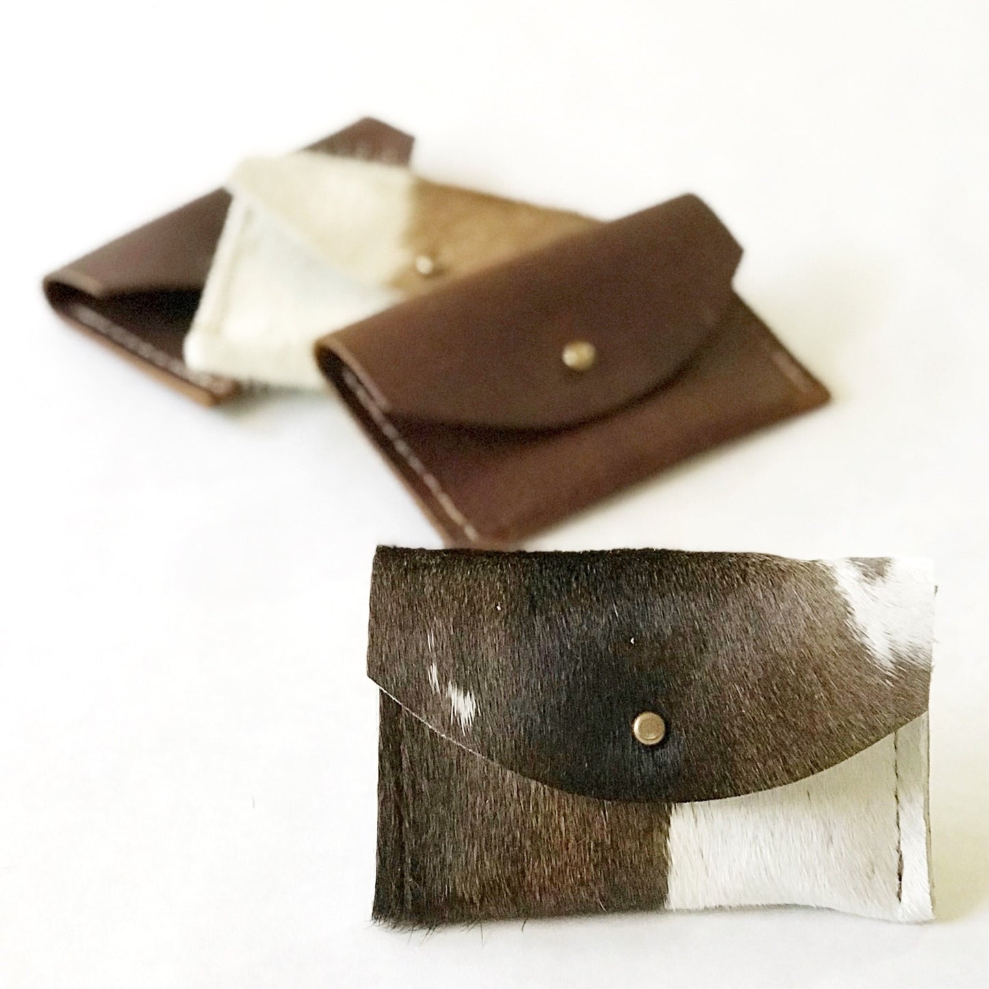 Cowhide and leather wallets with a central button on a white background