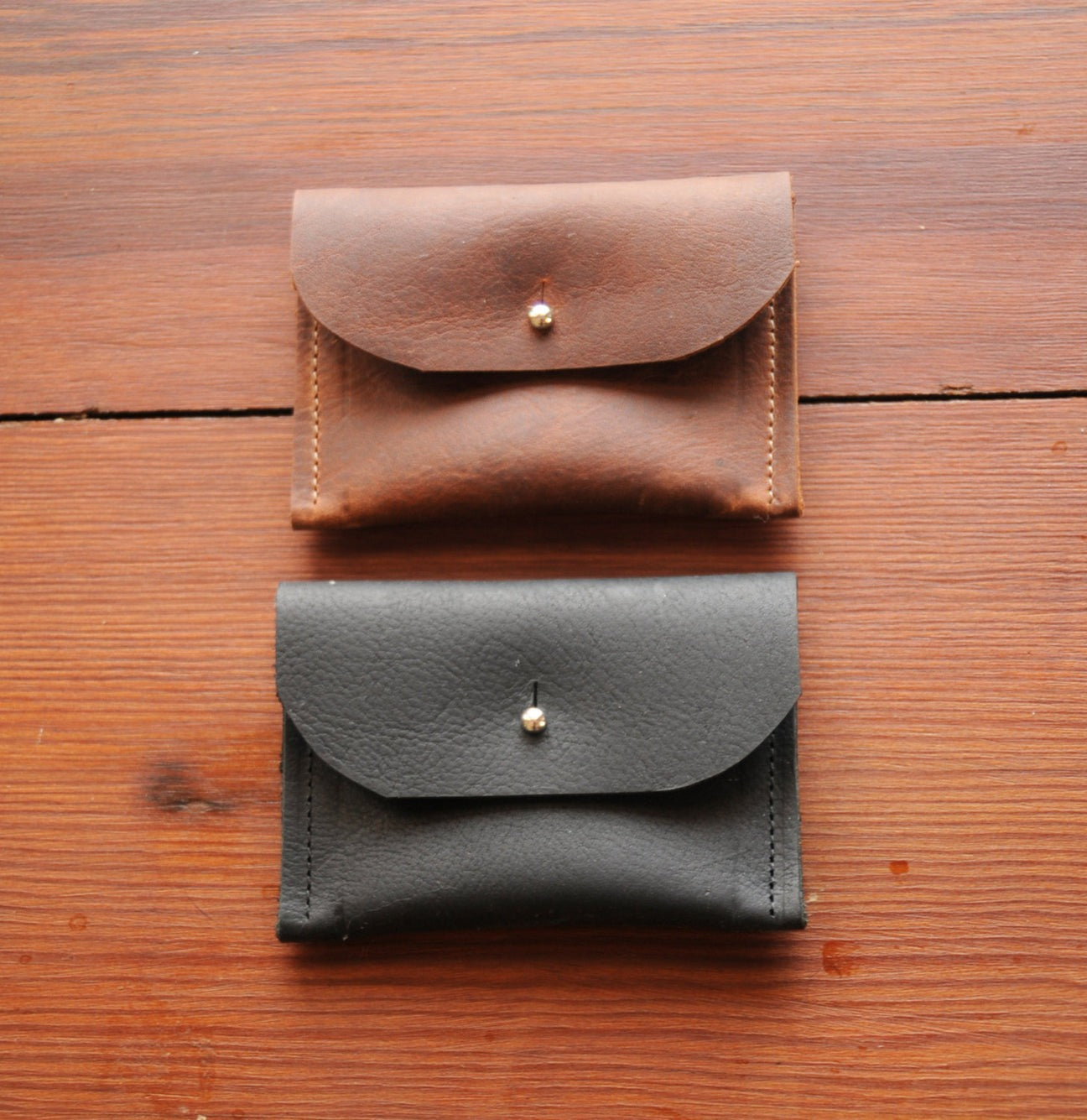 Two leather wallets, one brown and one black, on a wooden surface.