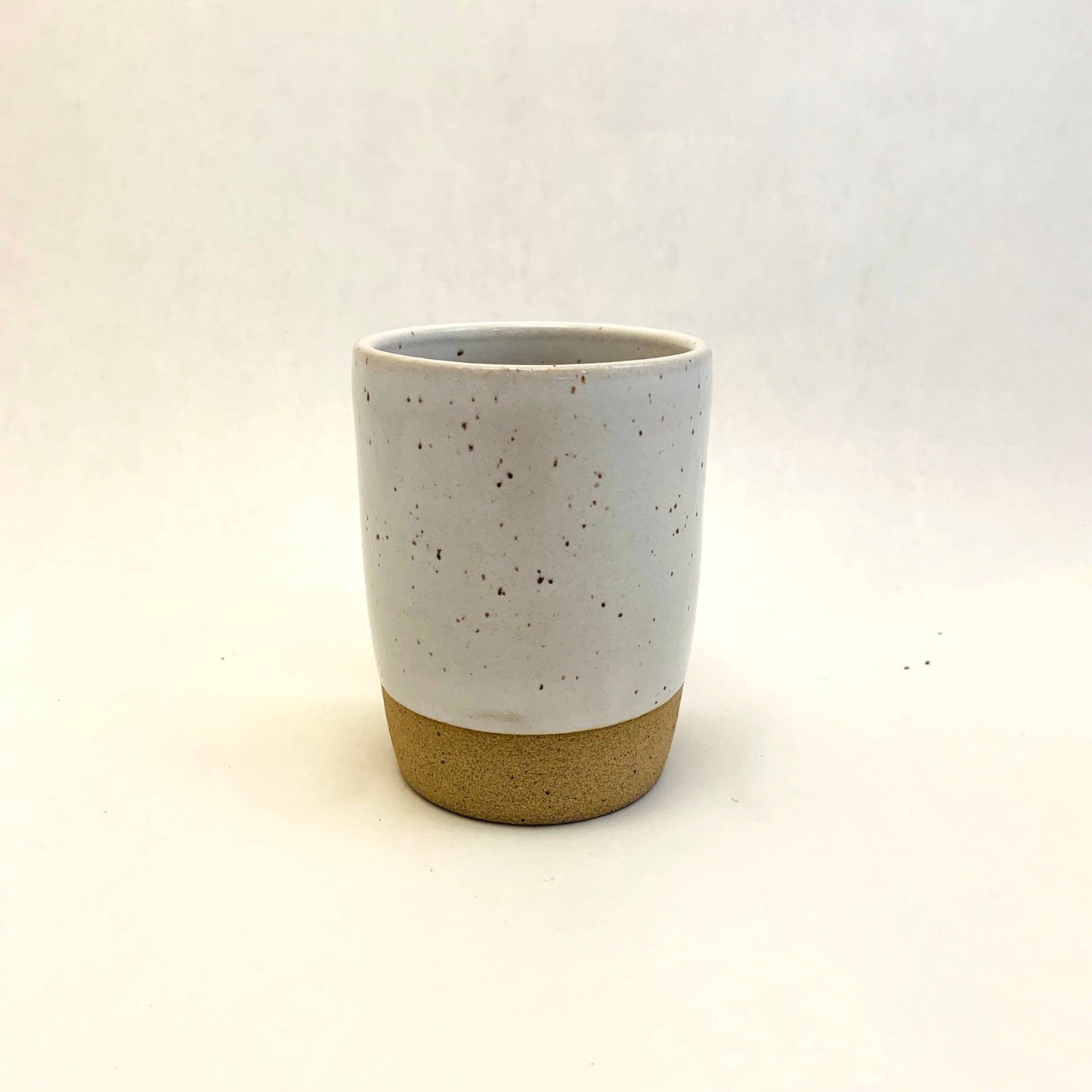 A beige ceramic tumbler with a solid pattern, approximately 3 1/2 inches tall, with a white speckled design upper half and a solid beige lower half.