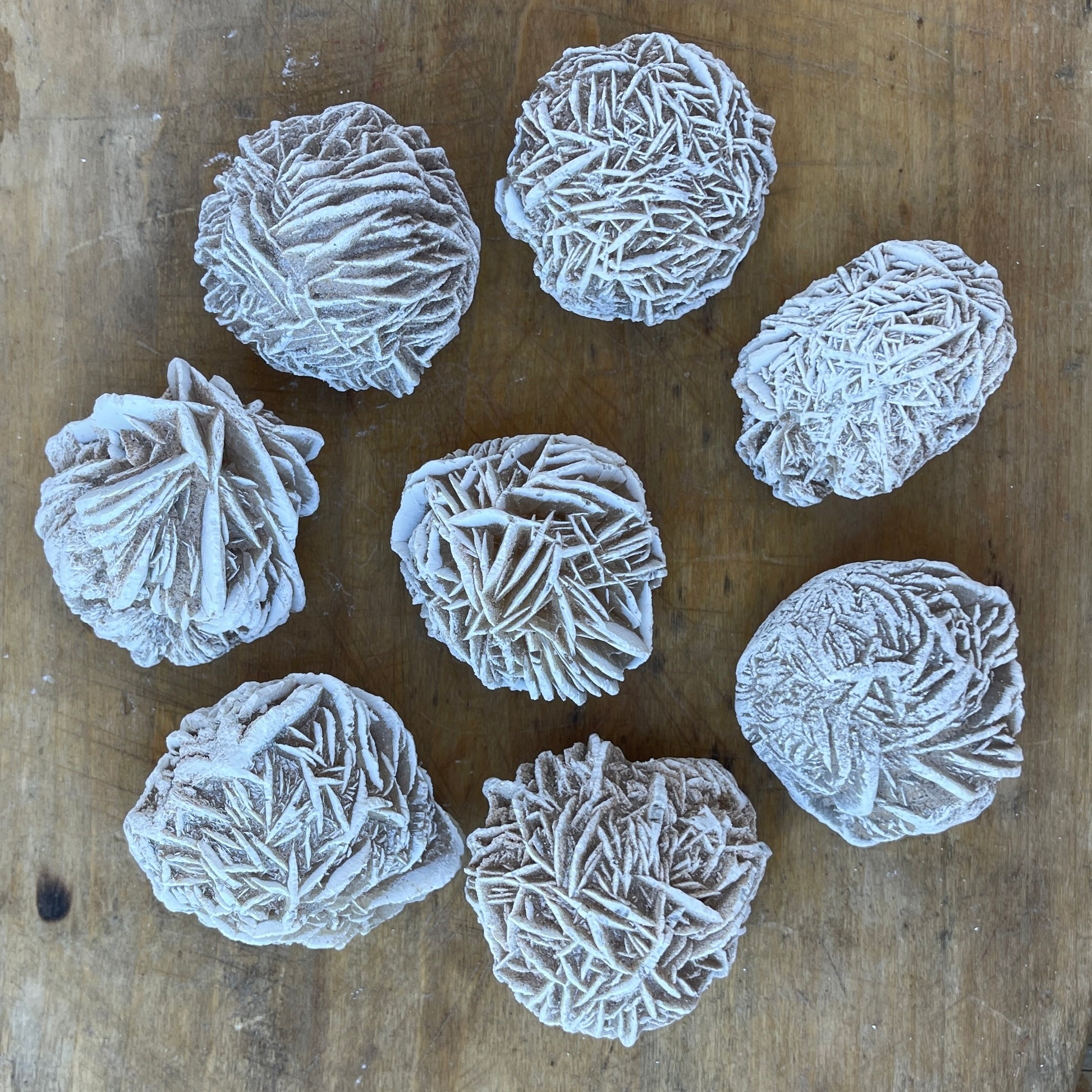 A collection of white desert rose selenite stones arranged on a wooden surface.