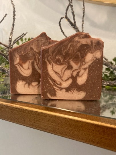 Two brown and beige marbled soap bars on a reflective surface with a natural background.