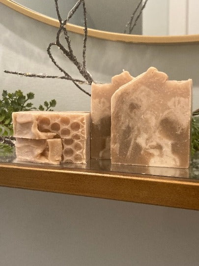 Three bars of soap with textured surfaces on a reflective surface, with a blurred background.