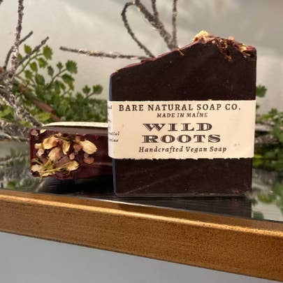 Bar of soap labeled 'Wild Roots' from Bare Natural Soap Co. on a wooden surface with a natural background.