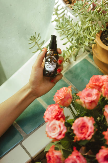 Hand holding a black spray bottle with a floral arrangement and plants in the background