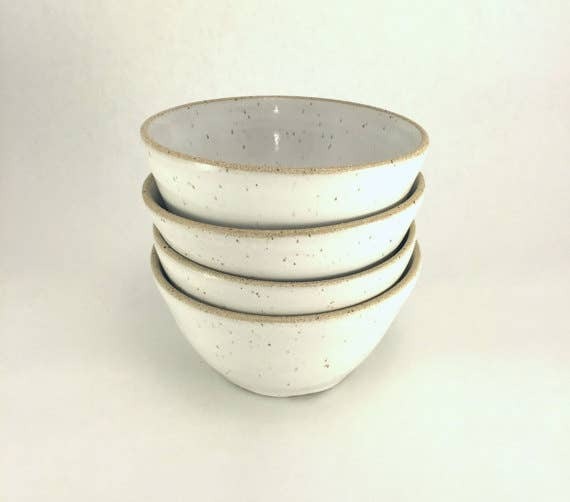 A stack of four beige ceramic bowls with a speckled pattern.