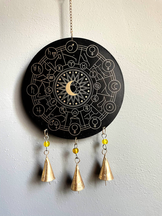 A black metal zodiac chime with gold-colored accents, featuring geometric patterns and moons, soldered together with protective color coating. It has small bell-like pendants and is displayed against a white background.