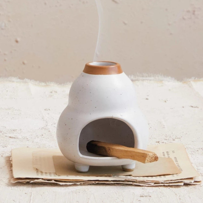 Ceramic incense burner with a single stick of incense on a textured surface.