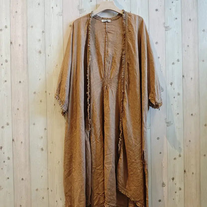 A loose, open-front kaftan-style tunic in a warm camel brown color, hanging on a wooden hanger against a light wood plank wall.