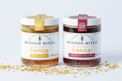 Two jars of Hudson Hives honey on a white background with scattered bee pollen.