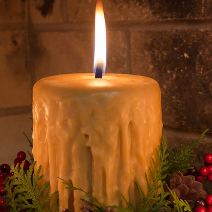 Candle with a flame surrounded by greenery and berries against a stone wall background