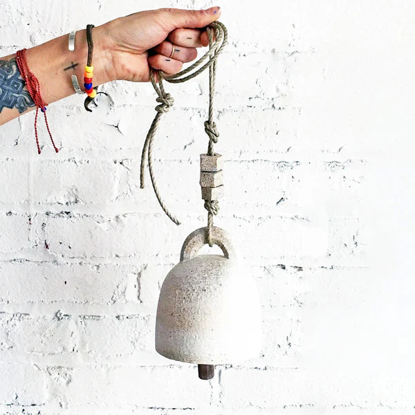 hand holding white ceramic bell from hemp rope
